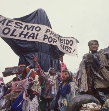 The photo shows the sculpture "Cristo Mendigo" that was the opening car of the Ratos e Urubus parade. In the image, the sculpture is covered in garbage bags as a censure, and carries the banner that reads "Even forbidden, watch over us!"