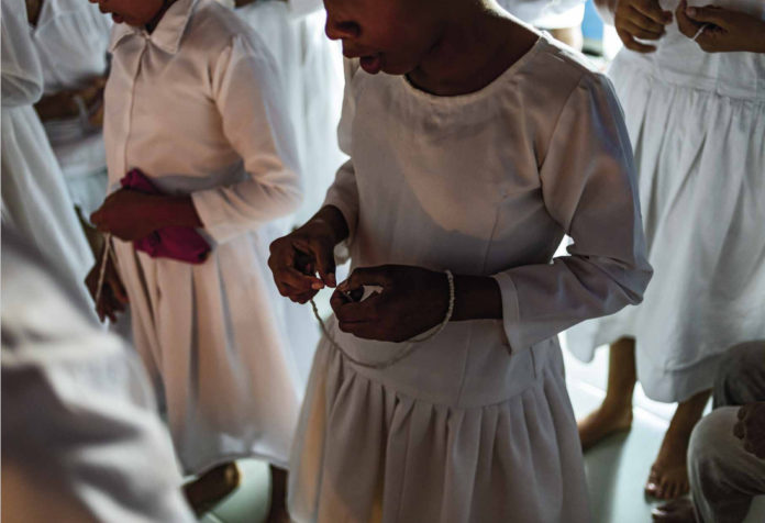 Meninas do Rosário de Virgem Maria da Boa Morte Meninas e mulheres vestindo hábitos claros rezam ave-marias com terços nas mãos