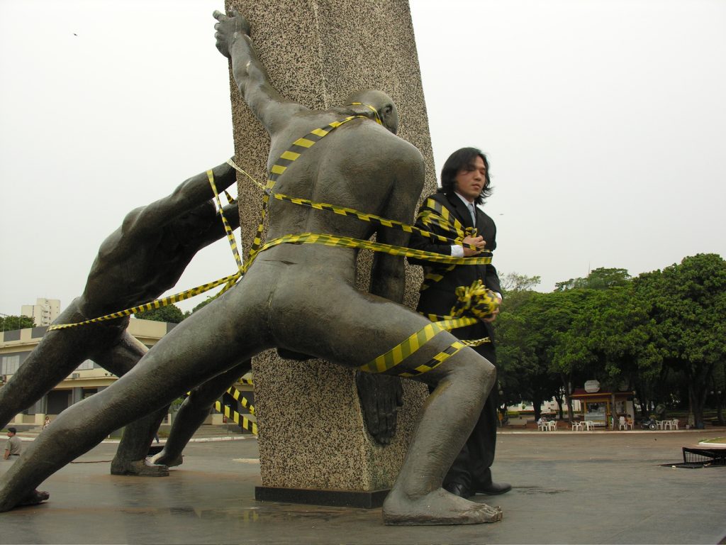 Performance "A quarta raça", na qual Shima se prendeu ao Monumento às Três Raças, em Goiânia, com fitas. 