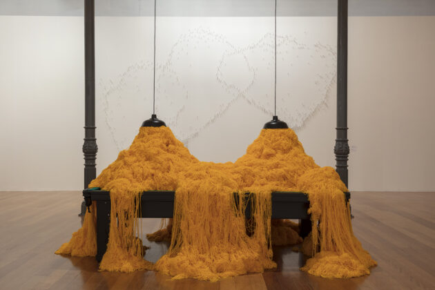 Foto horizontal, colorida. SNOOKER, uma mesa de sinuca recoberta de fios de lã que saem das luminárias dispostas acima dela.