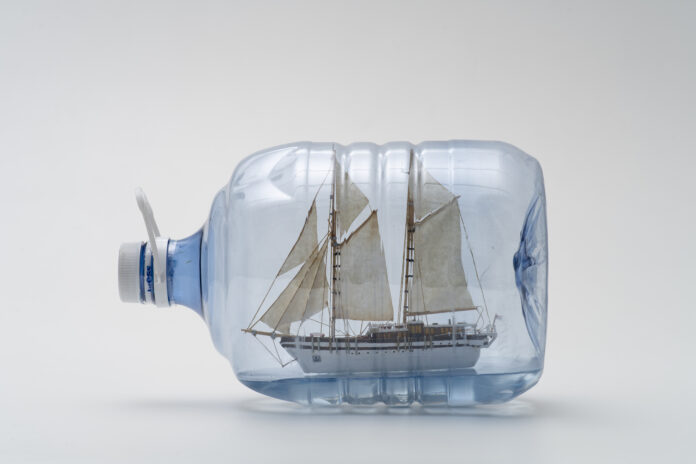 Horizontal, color image. Work DRIFT BOTTLE 7 (DRIFT TEST), by Jorge Macchi, a plastic bottle of mineral water that contains inside a reduced-scale reproduction of a sailboat
