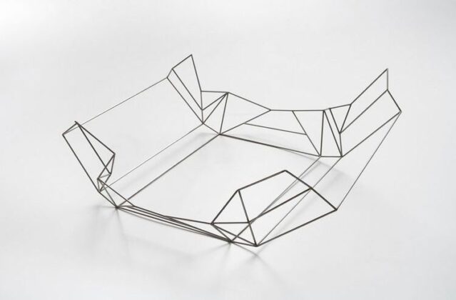 Horizontal, color image. Work from the PRESENTE series, by Jorge Macchi, structure made of a steel rod that reproduces the folds of a paper that at some point wrapped a box